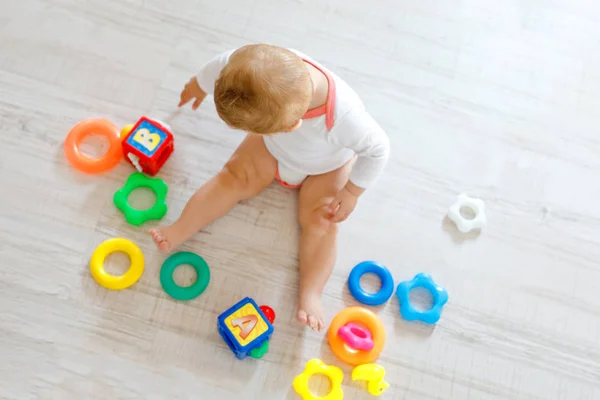 Bebek kız kreş eğitici oyuncaklar ile oynama. Mutlu sağlıklı çocuk evde renkli yumuşak oyuncaklar ile eğleniyor. Evlat plastik piramit inşa etmeye ve harflerle bloğu kullanma — Stok fotoğraf