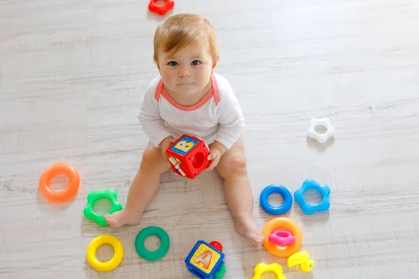 Schattig babymeisje spelen met de educatief speelgoed in de kinderkamer. Gelukkig gezond kind plezier met kleurrijke verschillende speelgoed thuis. Kind proberen kunststof piramide te bouwen en het gebruik van blokken met letters — Stockfoto