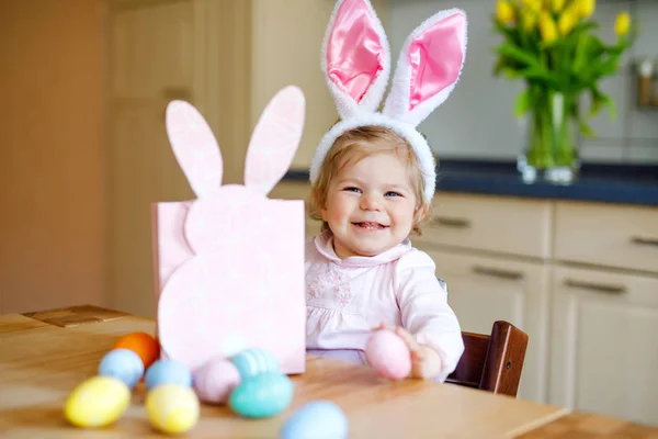 부활절 토끼 귀를 가진 귀여운 꼬마 소녀가 파스텔알을 가지고 놀고 있다. 선물을 포장하는 행복 한 아기. 가족 휴가를 즐기는 분홍색 옷을 입고 다정하게 웃는 건강 한 아이 — 스톡 사진