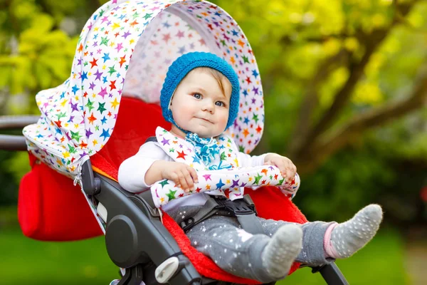 Bonito saudável pequena menina bonita com chapéu quente azul sentado no carrinho de bebê ou carrinho e esperando a mãe. Criança sorridente feliz com olhos azuis. bebê filha indo para um passeio com a família — Fotografia de Stock