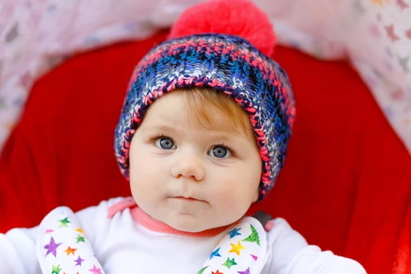 Bonito saudável pequena menina bonita com chapéu quente azul sentado no carrinho de bebê ou carrinho e esperando a mãe. Criança sorridente feliz com olhos azuis. bebê filha indo para um passeio com a família — Fotografia de Stock