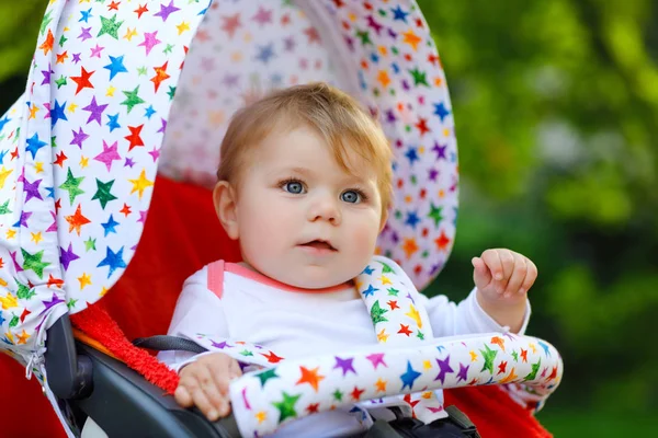 Cute healthy little beautiful baby girl sitting in the pram or stroller and waiting for mom. Happy smiling child with blue eyes. With green tree background. Baby daughter going for a walk with family — Stock Photo, Image