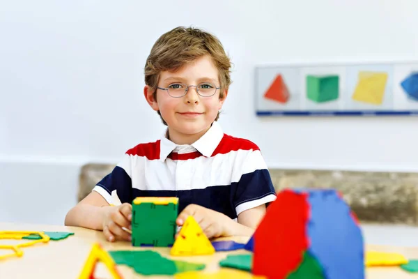 Happy kid boy with glasses having fun with building and creating geometric figures, learning mathematics and geometry — Stock Photo, Image