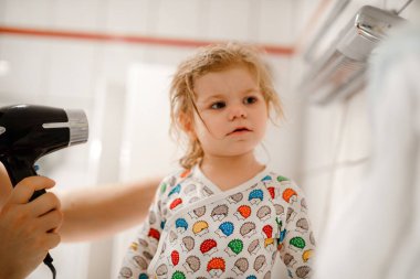 Babam saç kurutma makinesiyle küçük tatlı bir kızın saçlarını yapıyor. Banyo yaptıktan sonra ıslak saçlı sevimli sağlıklı bir bebek. Kızla babanın aile ilişkisi.