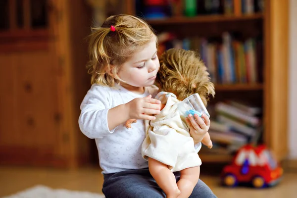 Adorável bonito pequena menina brincando com boneca. Criança bebê saudável feliz se divertindo com jogo de papel, jogando mãe em casa ou berçário. Filha ativa com brinquedo — Fotografia de Stock