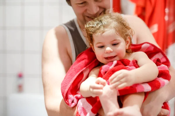 Vader met een schattig klein peutermeisje in een handdoek gewikkeld na het bad. Gelukkig gezond baby kind met natte haren kijken in de spiegel in de badkamer en lachen. Familierelatie van dochter en vader — Stockfoto