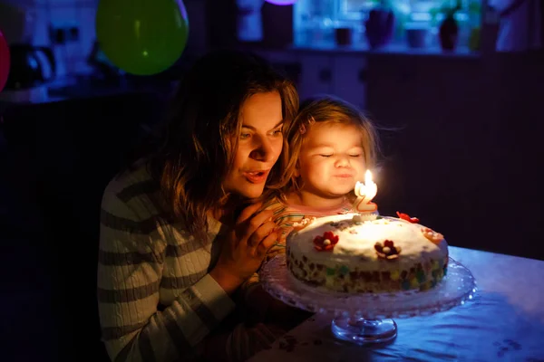 Imádnivaló baba kislány ünnepli második születésnapját. Baba gyermek lánya és a fiatal anya fúj a gyertyákat a tortán és a gyertyák. Boldog egészséges családi portré, az anya szerelem és a boldogság — Stock Fotó