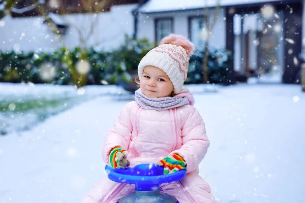 Söt liten småbarn flicka njuter av en släde rida på snö. Barnspann. Baby kid rider en släde i färgglada mode kläder. Utomhus aktivt roligt för familjen vintersemester på dagen med snöfall — Stockfoto