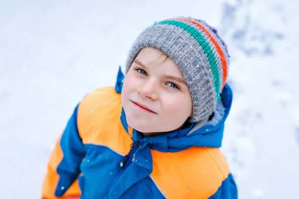 Portrait of little school kid boy in colorful clothes playing outdoors during snowfall. Active leisure with children in winter on cold snowy days. Happy healthy child having fun and playing with snow. — Stock Photo, Image