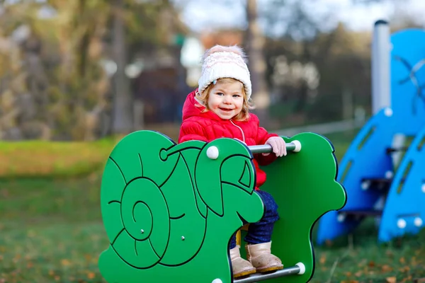 Linda niña que se divierte en el patio. Feliz niño sano escalando, balanceándose y deslizándose en diferentes equipos. En el día frío en ropa colorida. Juego activo al aire libre para niños — Foto de Stock