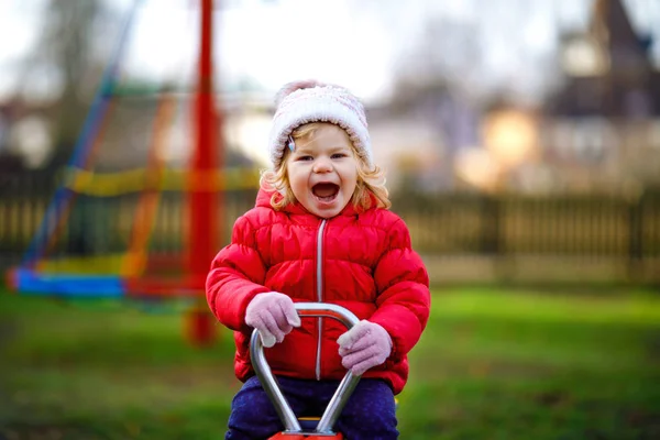 Nettes Kleinkind Mädchen hat Spaß auf dem Spielplatz. Glückliches gesundes kleines Kind klettern, schaukeln und rutschen auf verschiedenen Geräten. An kalten Tagen in bunten Klamotten. Aktives Outdoor-Spiel für Kinder — Stockfoto