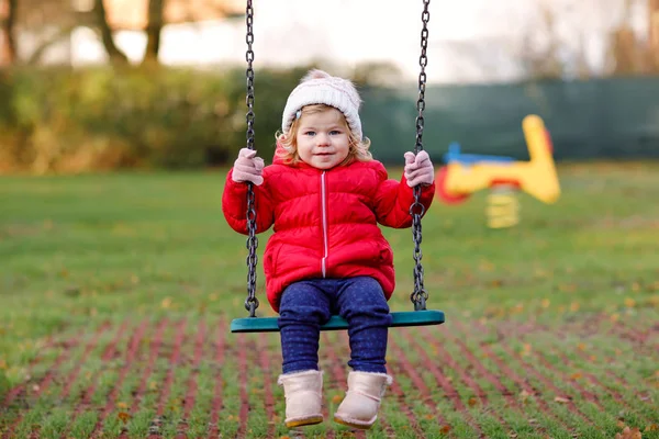 Söt liten flicka som har kul på lekplatsen. Glad frisk liten barn klättring, svänga och glida på olika utrustning. På kall dag i färgglada kläder. Aktivt utomhusspel för barn — Stockfoto