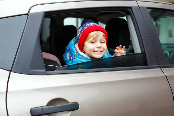 Portrait of pretty toddler boy sitting in car seat. Child transportation safety. Cute healthy kid boy looking happy about family vacations with car through window during standing in traffic jam — Stock Photo, Image