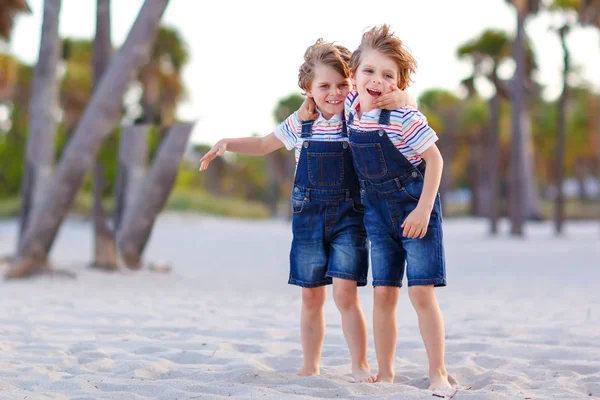 Deux petits enfants garçons s'amusent sur la plage tropicale, heureux meilleurs amis jouer, concept d'amitié. Frères frères et sœurs, jumeaux se battant, courant et sautant en famille regardez avec des palmiers sur le fond. — Photo