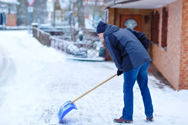Людина зі сніговою лопатою чистить тротуари взимку під час снігопаду. Зимовий час у Європі. Молодий чоловік у теплому зимовому одязі. Сніговий і погодний хаос у Німеччині. Снігопад і сильний сніг. Шнехаос — стокове фото