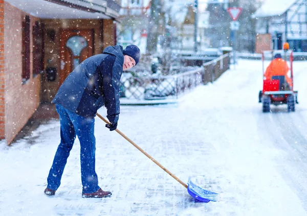 雪のシャベルを持つ男は雪の間の冬に歩道をきれいにする。ヨーロッパの冬時間。暖かい冬の服の若者。ドイツの雪と天気の混乱。吹雪と大雪。シュネカオス — ストック写真