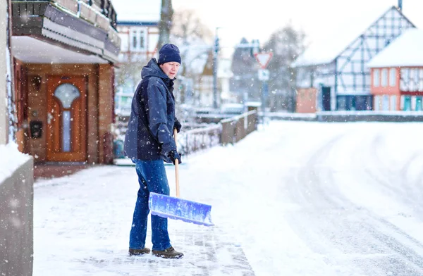 Kar kürekli bir adam kar yağışı sırasında kaldırımları temizler. Avrupa 'da kış mevsimi. Sıcak kış kıyafetleri giymiş genç bir adam. Almanya 'da kar ve hava kaosu. Kar fırtınası ve yoğun kar. Schneechaos — Stok fotoğraf