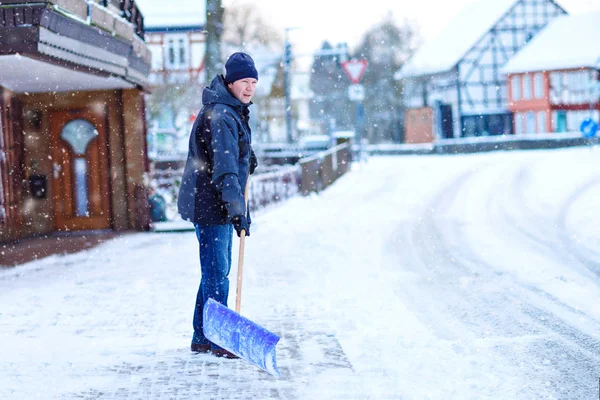 Człowiek z łopatą śnieżną czyści chodniki zimą podczas opadów śniegu. Czas zimowy w Europie. Młody człowiek w ciepłych zimowych ubraniach. Chaos śniegu i pogody w Niemczech. Burza śnieżna i silny śnieg. Schneechaos — Zdjęcie stockowe