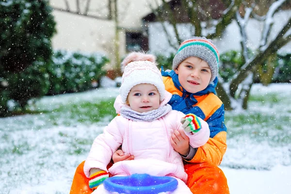 Little kid boy and cute toddler girl sitting together on sledge. Siblings, brother and baby sister enjoying sleigh ride during snowfall. Children sledding on snow. Active fun for family vacation — Stock Photo, Image