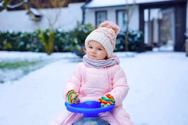 Söt liten småbarn flicka njuter av en släde rida på snö. Barnspann. Baby kid rider en släde i färgglada mode kläder. Utomhus aktivt roligt för familjen vintersemester på dagen med snöfall — Stockfoto