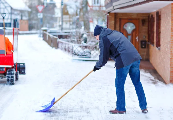 Людина зі сніговою лопатою чистить тротуари взимку під час снігопаду. Зимовий час у Європі. Молодий чоловік у теплому зимовому одязі. Сніговий і погодний хаос у Німеччині. Снігопад і сильний сніг. Шнехаос — стокове фото