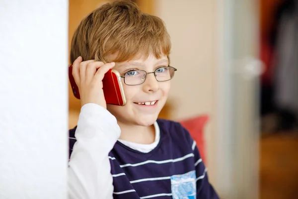 Un ragazzino carino con gli occhiali da vista che parla al cellulare. Adorabile bambino sano in possesso di smartphone e parlare con una ragazza amica o con i genitori, nonni. — Foto Stock