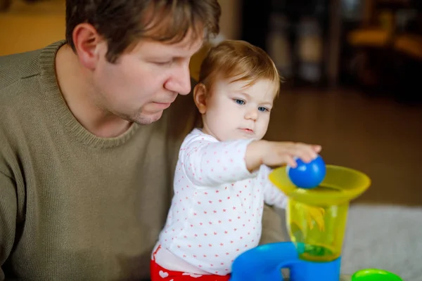 Glada stolta unga far ha kul med baby dotter, familjeporträtt tillsammans. Pappa leker med flicka med pedagogiska sorterare leksak med olika färgglada bollar. Man med små barn hemma. — Stockfoto