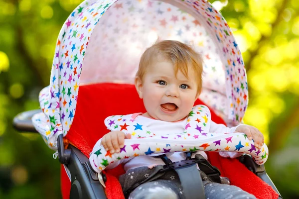Cute healthy little beautiful baby girl sitting in the pram or stroller and waiting for mom. Happy smiling child with blue eyes. With green tree background. Baby daughter going for a walk with family — Stock Photo, Image