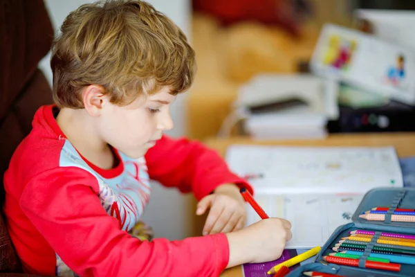 Porträt eines süßen, glücklichen Schuljungen, der zu Hause Hausaufgaben macht. Kleines Kind schreibt mit Buntstiften, drinnen. Grundschule und Bildung. Kind lernt Buchstaben und Zahlen schreiben — Stockfoto