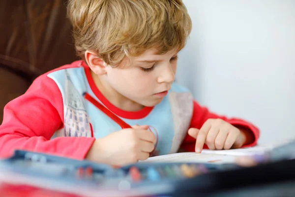 Retrato de lindo niño de la escuela feliz en casa haciendo tarea. Niño pequeño escribiendo con lápices de colores, en el interior. Escuela primaria y educación. Niño aprendiendo a escribir letras y números —  Fotos de Stock