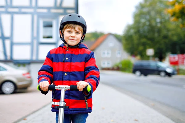 Schattig klein schoolkind jongen met helm rijden op scooter in park natuur. activiteiten voor kinderen in de buitenlucht in de winter, lente of herfst. grappig gelukkig kind in kleurrijke mode kleding. — Stockfoto