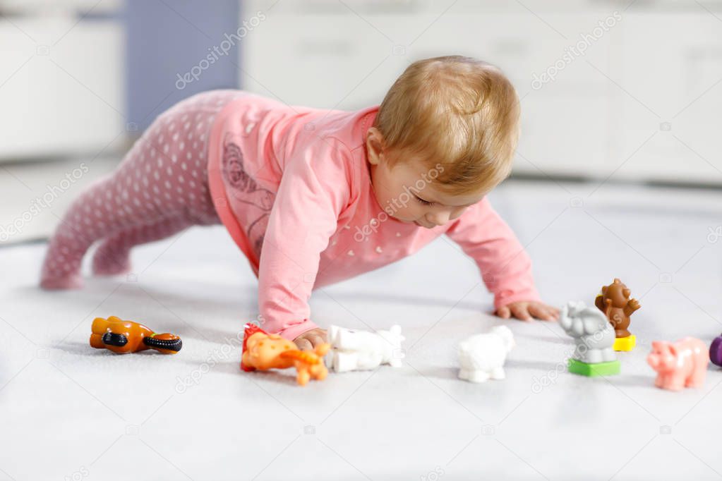 Adorable baby girl playing with domestic toy pets like cow, horse, sheep, dog and wild animals like giraffe, elephant and monkey. Happy healthy child having fun with colorful different toys at home