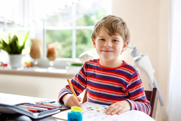 Szczęśliwy uśmiechnięty chłopczyk w domu odrabiający lekcje rano, zanim zacznie się szkoła. Małe dziecko ćwiczy, w domu. Szkoła podstawowa i edukacja: Rysunek figur geometrycznych chłopca — Zdjęcie stockowe