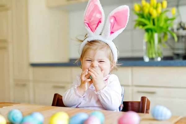 Cute little toddler girl wearing Easter bunny ears playing with colored pastel eggs. Happy baby child unpacking gifts. Adorable kid in pink clothes enjoying holiday — Stock Photo, Image