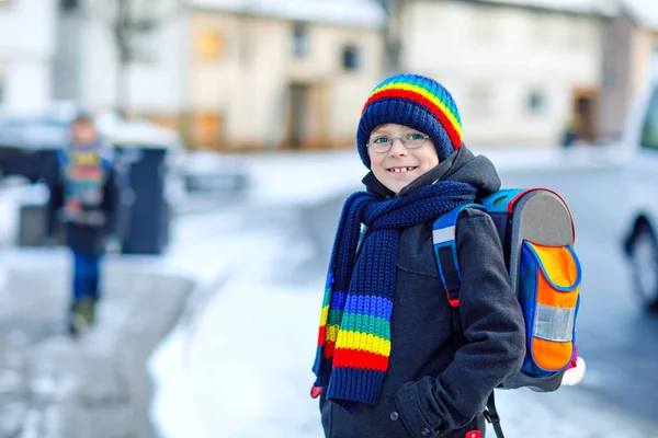 Two little kids boys of elementary class walking to school during snowfall. Happy children having fun and playing with first snow. Siblings ans friends with backpack in colorful winter clothes. — Stock Photo, Image