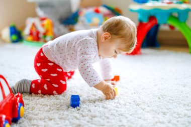 Küçük şirin bebek kız tarama öğrenme. Sağlıklı çocuk çocuk odası renkli oyuncaklar ile kaynıyor. Bebek bacakları arkadan görünüm. Ana sayfa keşfetmek ve farklı becerileri öğrenme şirin bebek