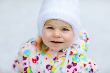 Kışın dışarıda yürüyen küçük bir kızın portresi. Tatlı bebek lolipop şekeri yiyor. Soğuk kar gününde eğlenen bir çocuk. Ilık bebek kıyafetleri ve boncuklu şapkası vardı..