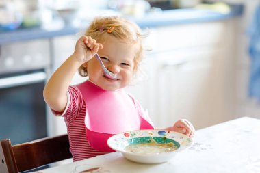 Sevimli bebek kaşık sebze çorbası içiyor. Yemek, çocuk, beslenme ve gelişim konsepti. Sevimli çocuk, kaşıklı kız sandalyede oturuyor ve kendi kendine yemek yemeyi öğreniyor.