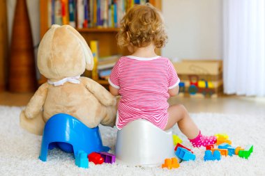 Closeup of cute little 12 months old toddler baby girl child sitting on potty. Kid playing with big plush soft toy. Toilet training concept. Baby learning, development steps clipart