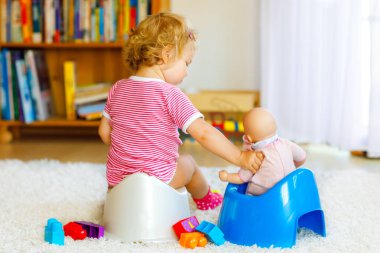 Closeup of cute little 12 months old toddler baby girl child sitting on potty. Kid playing with doll toy. Toilet training concept. Baby learning, development steps clipart