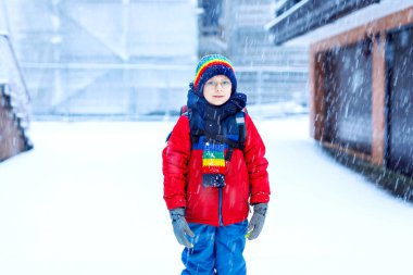 Gözlüklü mutlu çocuk okula giderken karla eğleniyor.