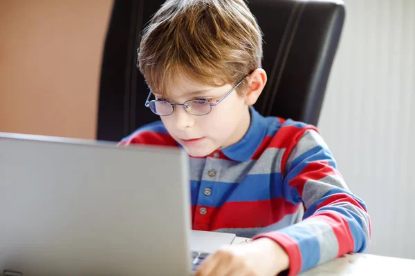 Счастливый здоровый мальчик с очками, делающий домашнюю работу дома с тетрадью. Заинтересованный ребенок пишет эссе с помощью Интернета. Концепция скрытых школьников — стоковое фото