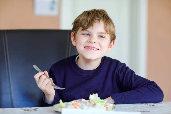 Gelukkige jongen die verse salade eet met tomaat, komkommer en verschillende groenten als maaltijd of snack. Gezond kind genieten van lekker en vers eten thuis of op school kantine. — Stockfoto