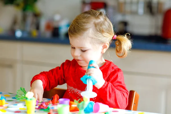 Очаровательная милая маленькая девочка с красочной глиной. Здоровый ребенок играет и создает игрушки из теста. Маленький ребенок моделирует когти и учится — стоковое фото
