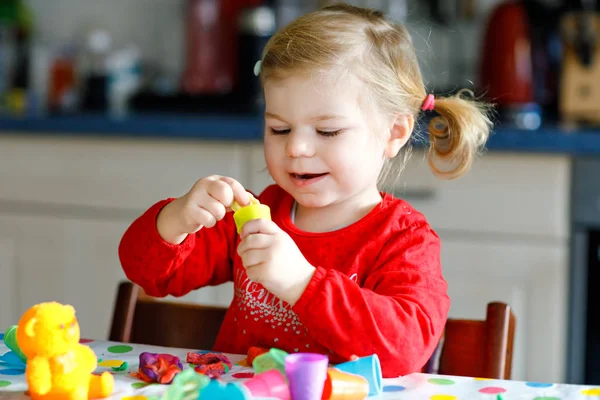 Aranyos kis aranyos kislány színes agyaggal. Egészséges gyermek játszik, és játékokat hoz létre játék tészta. Kisgyerek formázás modellezés agyag és a tanulás — Stock Fotó