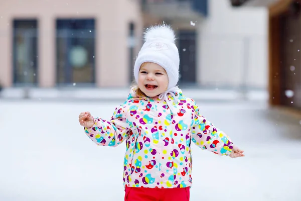 Porträtt av en liten flicka som går utomhus på vintern. Söta småbarn som äter sött godis. Barn har roligt på kall snö dag. Bär varm baby färgglada kläder och hatt med kulor. — Stockfoto