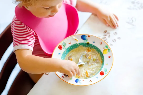 Menina close-up comendo de sopa de macarrão vegetal colher. conceito de alimentação, criança, alimentação e desenvolvimento. close-up da criança, filha com colher sentada em cadeira alta e aprendendo a comer por si só — Fotografia de Stock