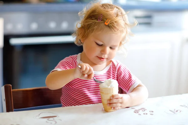 Menina adorável comendo de colher sorvete doce em cone de waffle. conceito de alimentação, criança, alimentação e desenvolvimento. Criança bonito, filha com colher sentada em cadeira alta e aprendendo a comer por si só — Fotografia de Stock