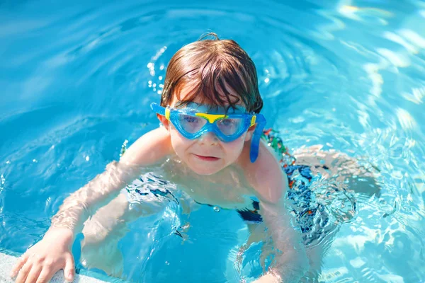 Un bambino in età prescolare che fa sport di nuoto. Ragazzo con gli occhiali da nuoto che raggiungono il bordo della piscina. Bambino che si diverte in piscina. Bambino felice attivo che vince. sport, tempo libero attivo . — Foto Stock