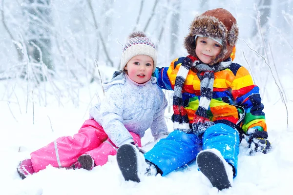 Dois meninos e meninas bonitos na floresta nevada de inverno no fundo flocos de neve. lazer ao ar livre e estilo de vida com crianças em dias de neve fria. Irmãos felizes, irmão e irmã brincando — Fotografia de Stock